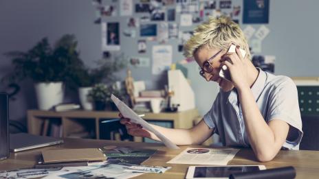 Short-haired woman on the phone surrounded by papers 