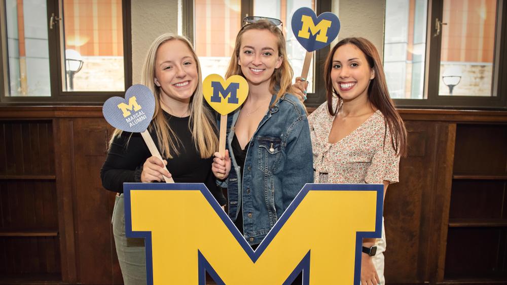 Three students smiling behind a Marsal Family sign