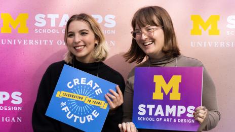 Two Stamps students hold signs that read Create the Future, Stamps School of Art & Design, and friends