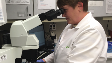 A woman in a white coat uses a microscope 