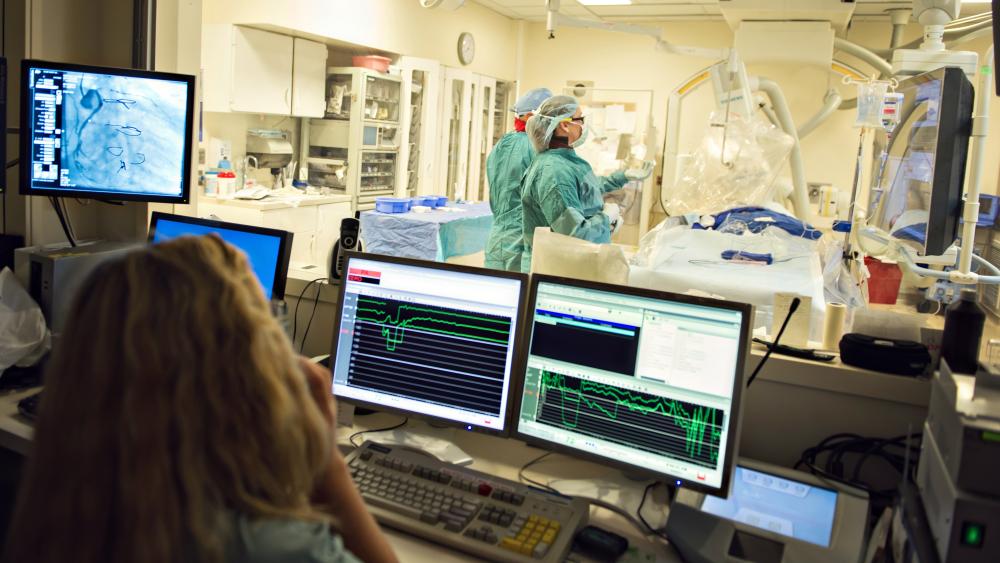 View from observation room with computer screens into a procedure room with medical professionals