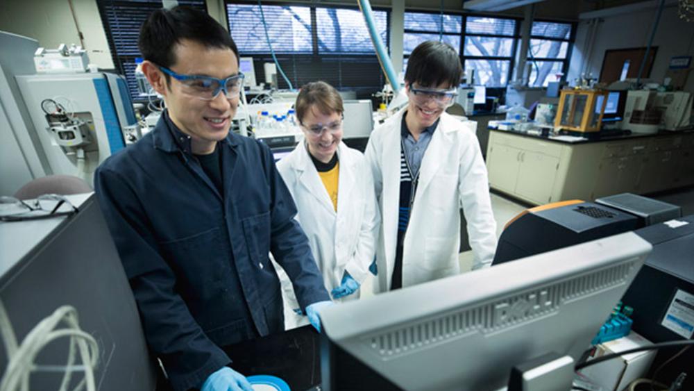 PhD students surround a computer in a lab