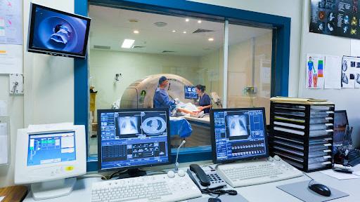 A patient enters an MRI machine while monitors and screens showcase images.