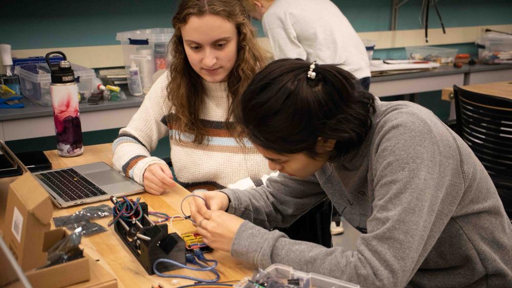 Two female undergraduate students work with wires for creating prototype for ME 450 project.