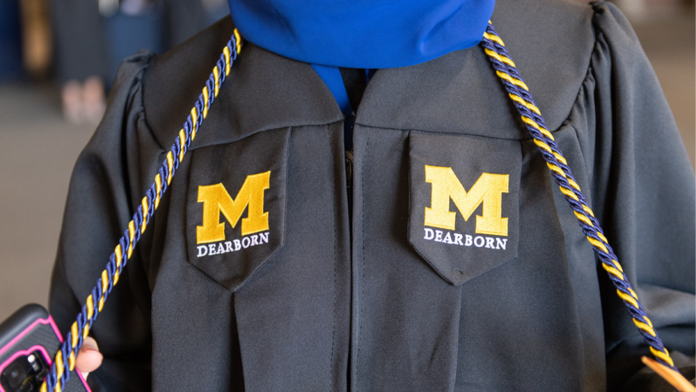 Student wearing graduation gown with embroidered UM-Dearborn logo