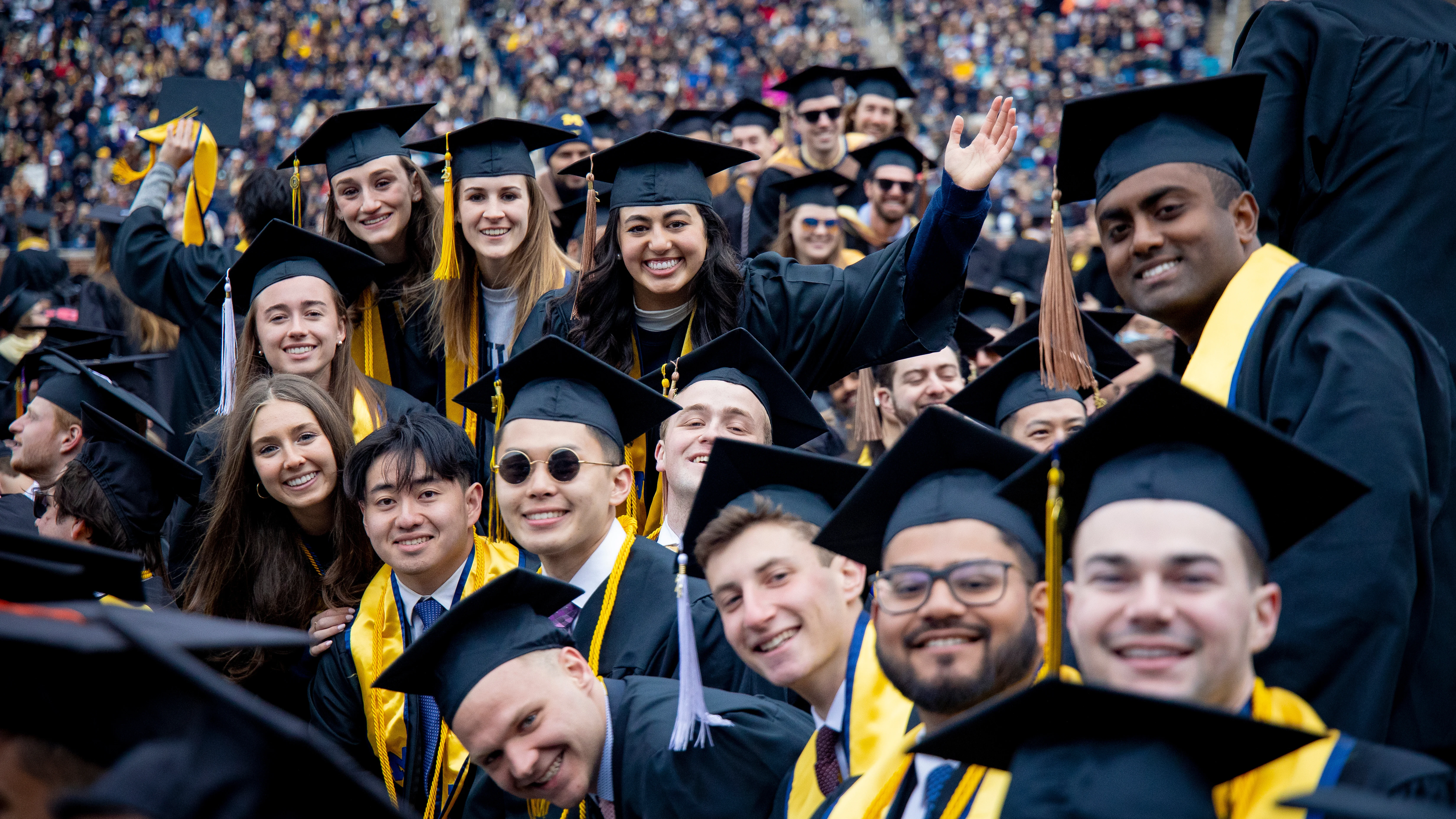 Graduates in cap and gown smiling and waving 