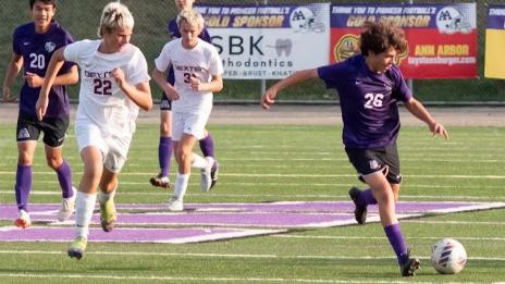 Elliott kicks a soccer ball down the field at his charity game while other players run alongside. 