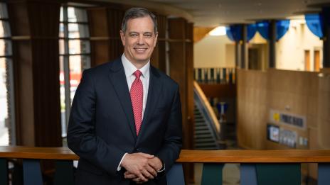 Dean Charles Holmes smiles while leaning against a balcony railing.
