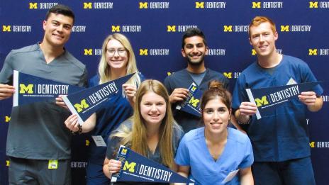 A group of students wearing scrubs and posing with dentistry branded pennants 