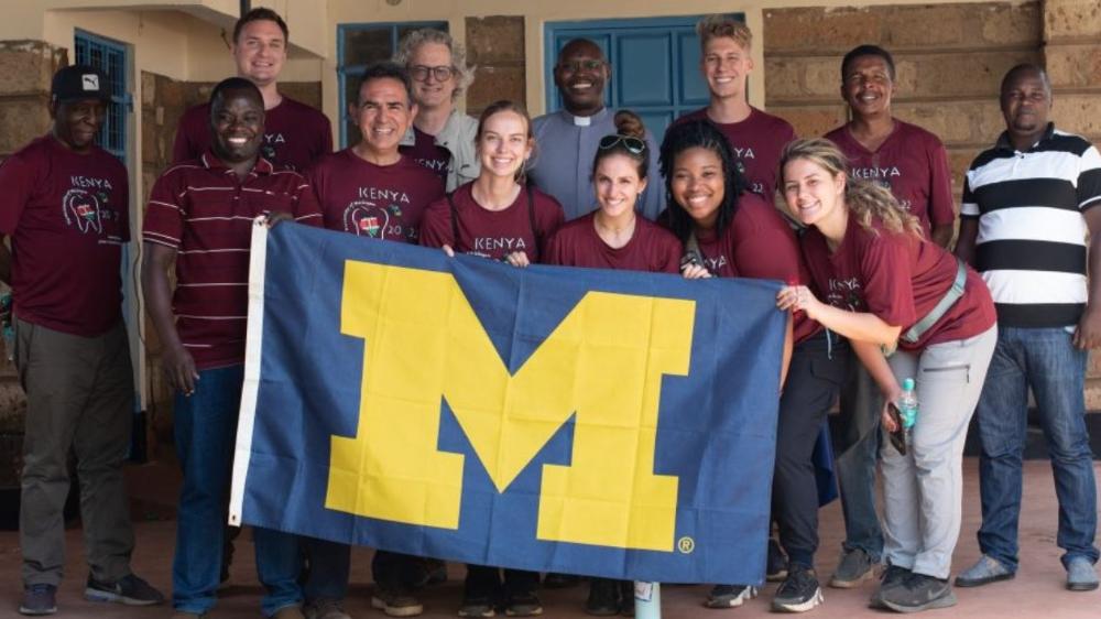 Members of the School of Dentistry outreach team pose with teachers and drivers in Kenya holding a UM flag 