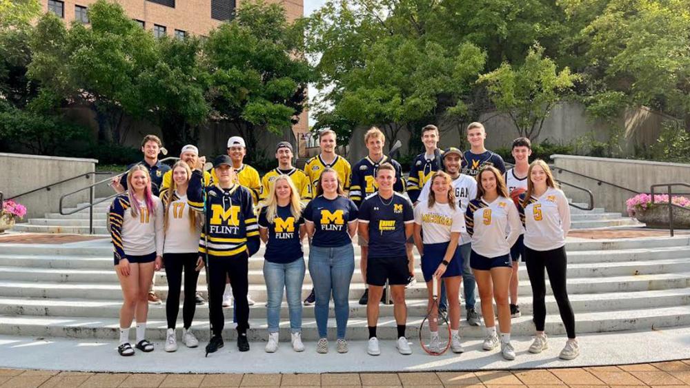 Athletes from most UM-Flint’s clubs sports, wearing uniforms, practice gear, and UM-Flint t-shirts pose on steps on campus.