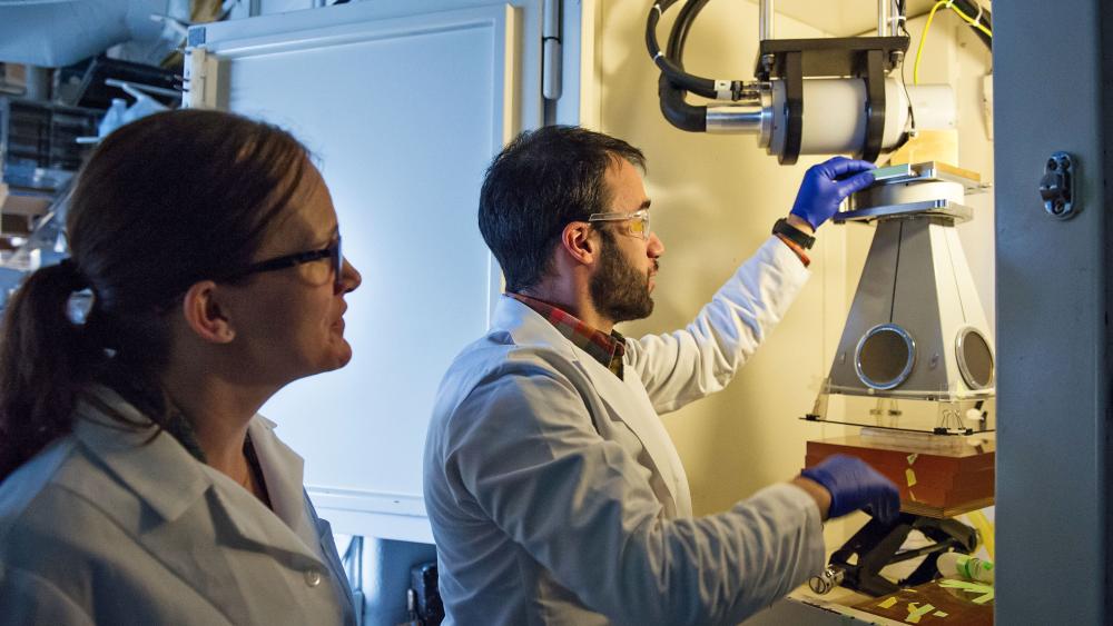 A female medical professional observes a male medical professional working with medical equipment