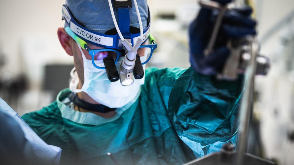 Up close of a male medical professional wearing personal protection equipment, head light, and magnifying glasses in an operating room