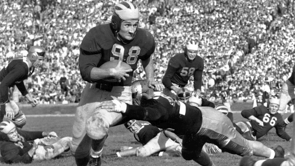 Black and white photo of man with football running down the field while players try to tackle him