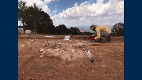 A man crouches to inspect findings uncovered in the ground at an archaeological site.