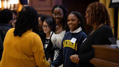 A few students in a group smiling and one is shaking hands with a woman.