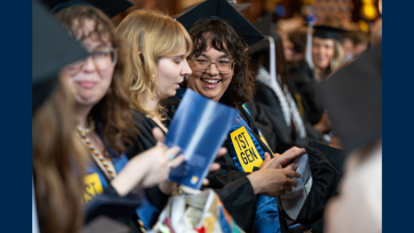 Students in cap and gown at graduation laugh together