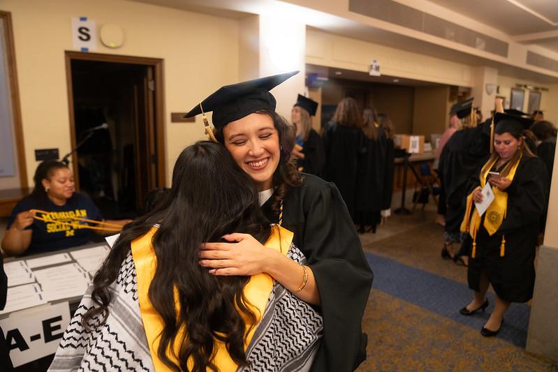 School of Social Work graduate hugging friend at commencement ceremony with her cap and gown.