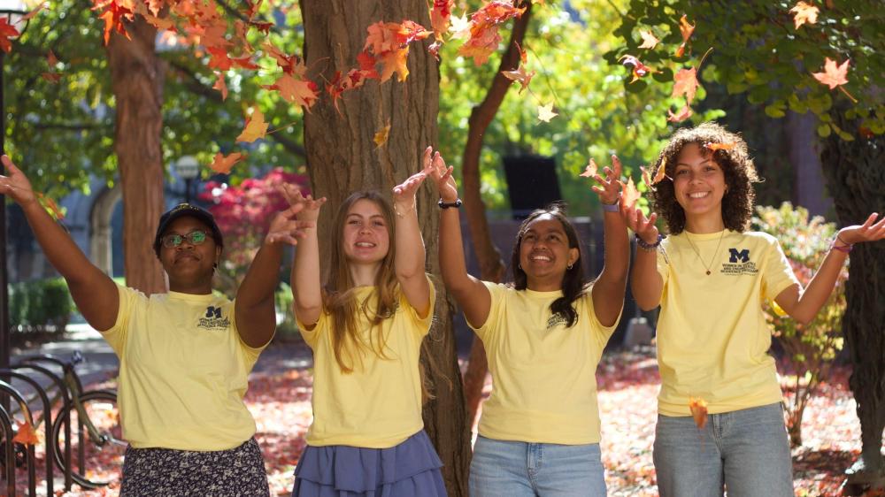 Four WISE RP students in their yellow WISE RP shirts outside during the Fall throwing leaves. 