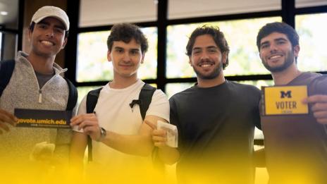 Four University of Michigan students gathered together and smiling. Two are holding up information that promotes voter engagement.