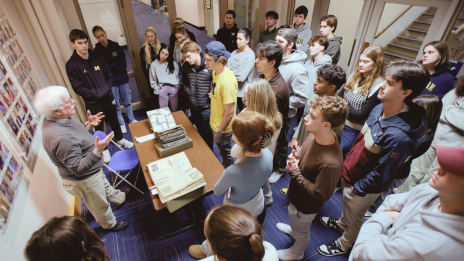 Students gathered around a table looking at old books and photos.