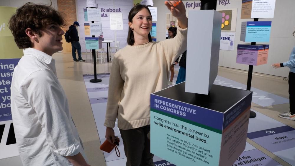 Two Students stand in front of ballot wayfinder signage